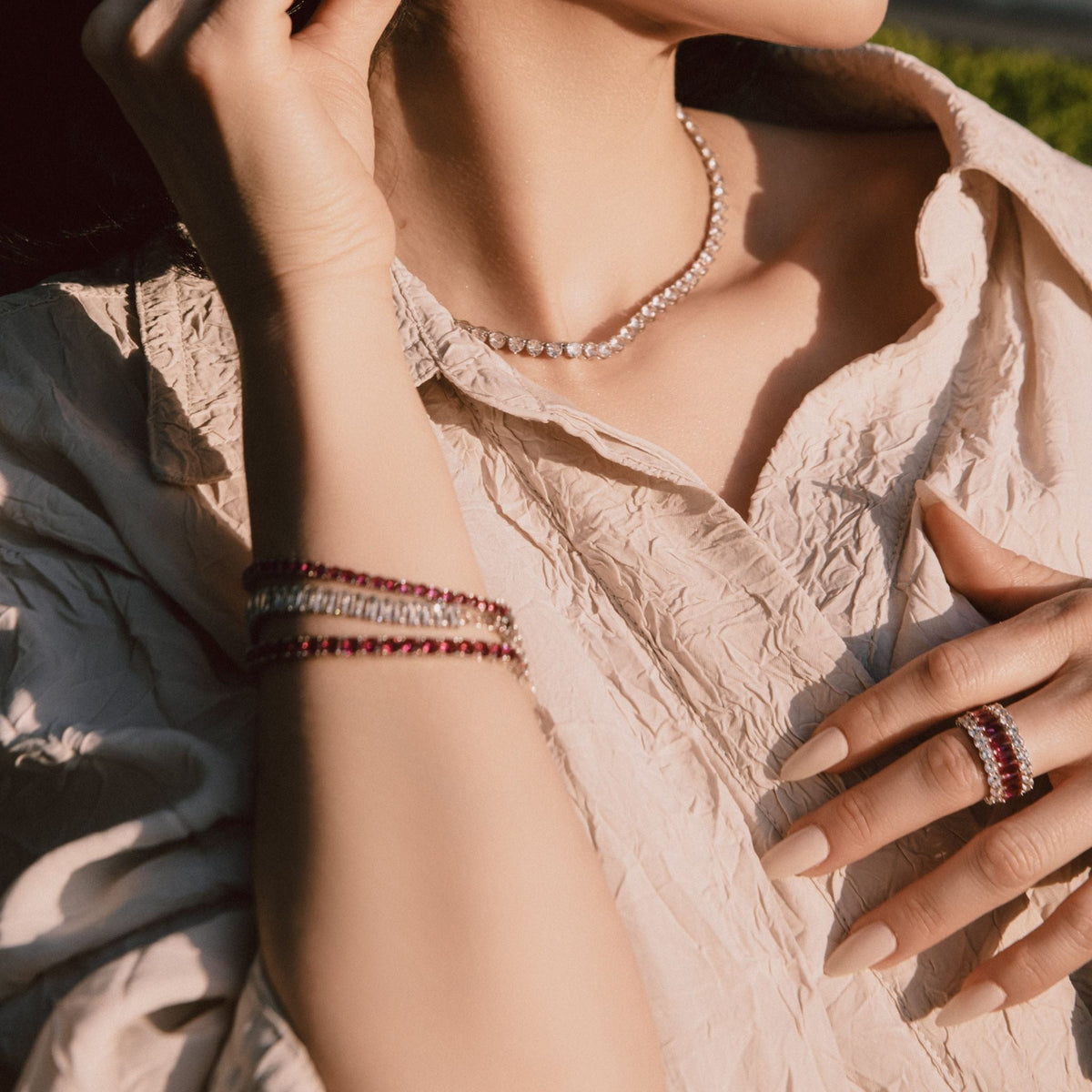 Close-up of a person wearing a necklace, bracelet, and ring with a blurred natural background