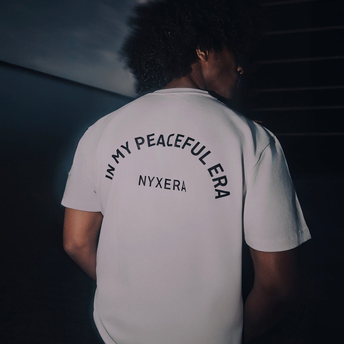 Person wearing a white t-shirt with text on the back in a dark setting