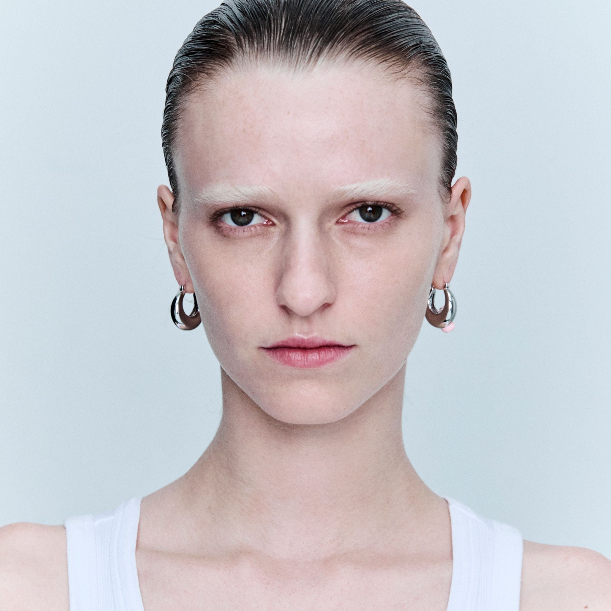 Person wearing hoop earrings against a light gray background