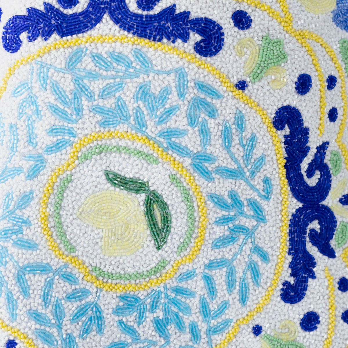 Close-up of SELF-ADORE’s Limoncello Hand-Beaded Embellished Mini Dress in White/Blue, with blue swirls, yellow accents, green leaves, and a central lemon-like motif on a white background.