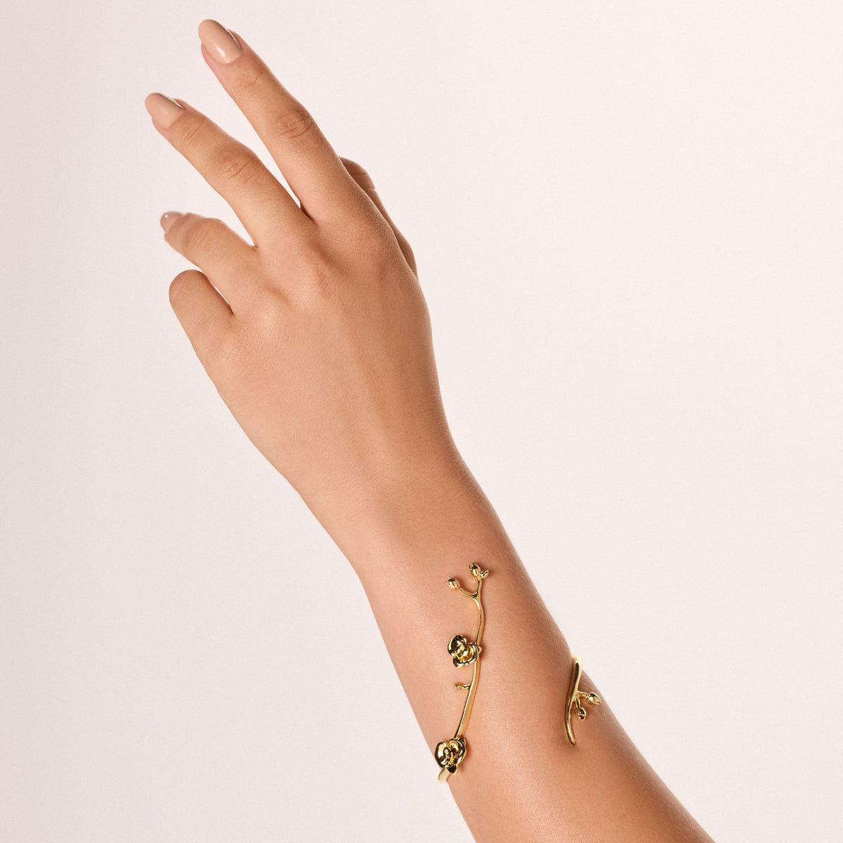 A hand with a neutral manicure is raised gracefully, showcasing the Gold Floralis Bracelet from ANNA PRATA's AFlora Collection—a delicate, contemporary romantic piece inspired by vines and small flowers, set against a light background.