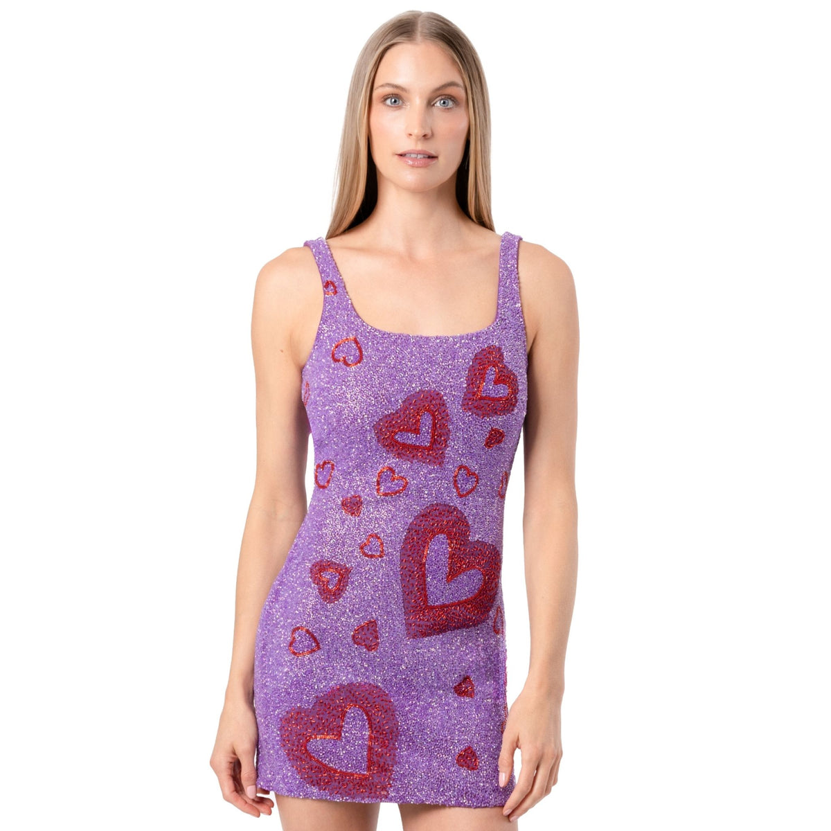 A woman with straight, light brown hair wears the SELF-ADORE Lust Hand-Beaded Embellished Mini Dress, a sleeveless sparkly purple mini dress adorned with red glitter hearts. She stands facing forward against a plain white background.