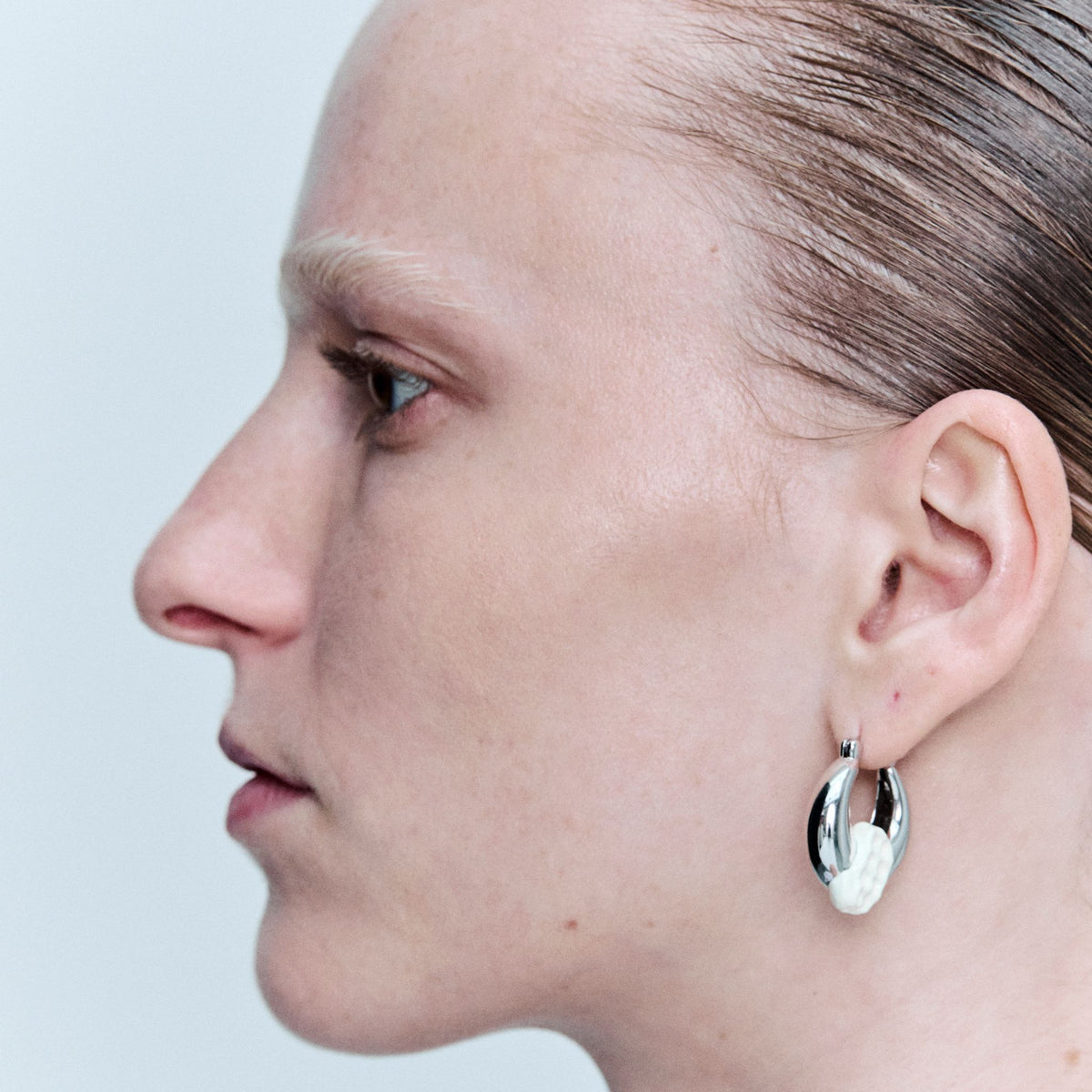 Close-up of a person wearing a silver hoop earring on a light gray background