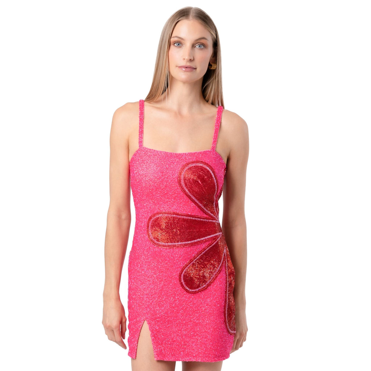 A woman models the SELF-ADORE Bloom Hand-Beaded Embellished Mini Dress—sparkly, pink, with thin straps and a large red statement flower—standing against a plain white background.