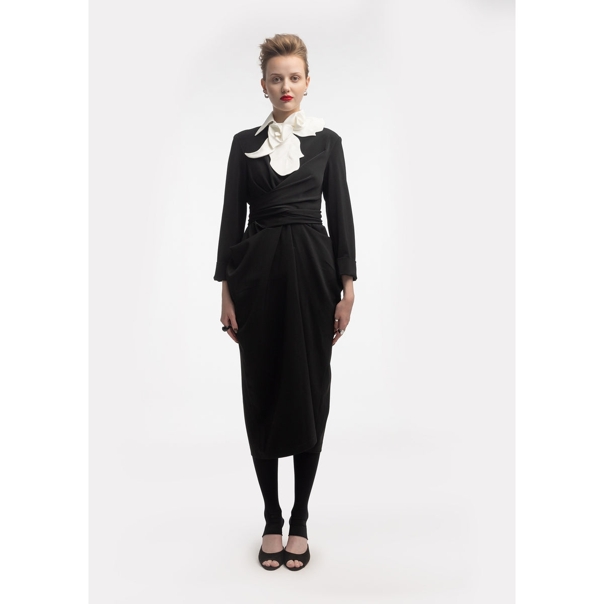 A woman faces forward in a fitted black dress and JULIA ALLERT’s Designer Neckwear - Collar in white. She wears red lipstick, has short styled hair, black leggings, open-toe black shoes, and stands against a plain white background.