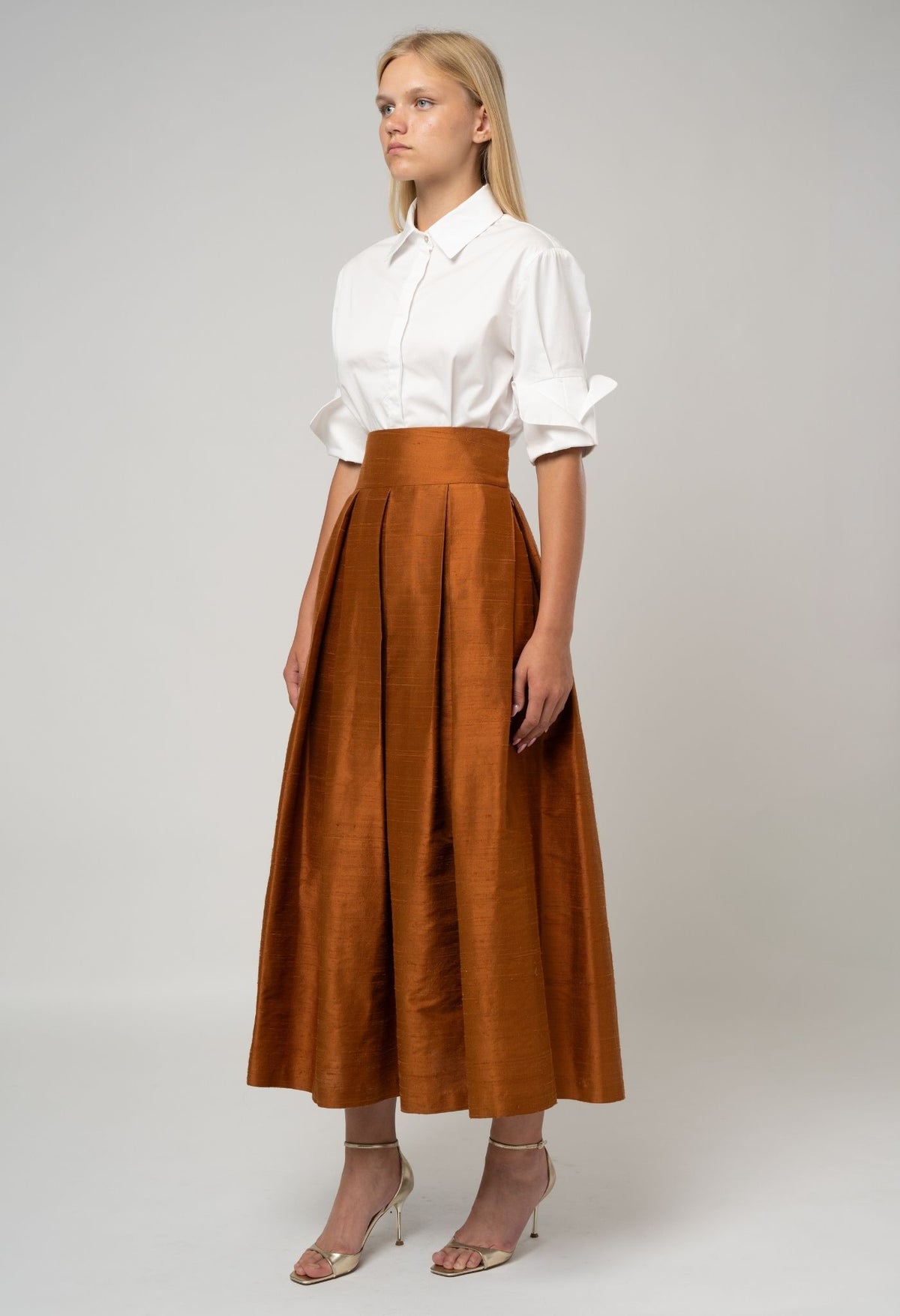 Woman wearing a white blouse and brown skirt on a plain background