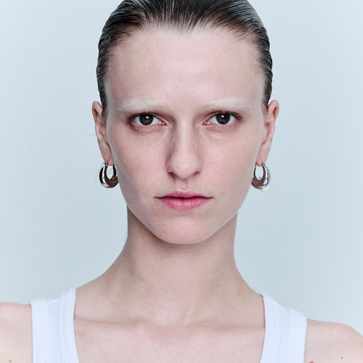 Person wearing hoop earrings against a light gray background