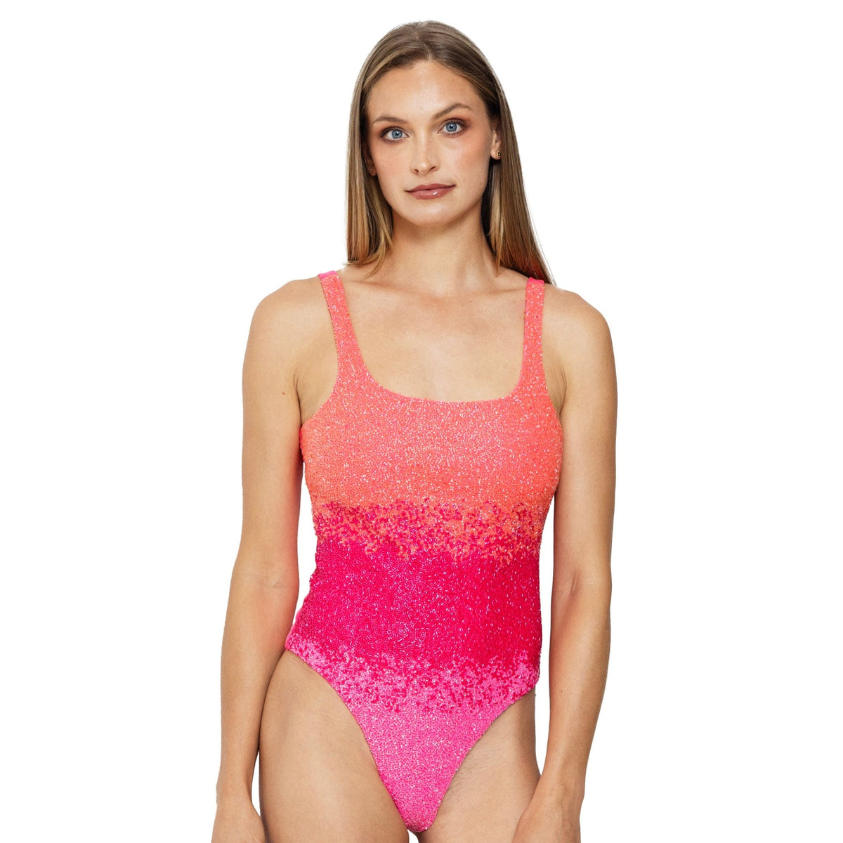 A woman with long, straight blonde hair wears the SELF-ADORE Ombre Hand-Beaded Embellished One-Piece Swimsuit, a sleeveless design with a coral orange to bright pink gradient, standing facing forward against a white background.