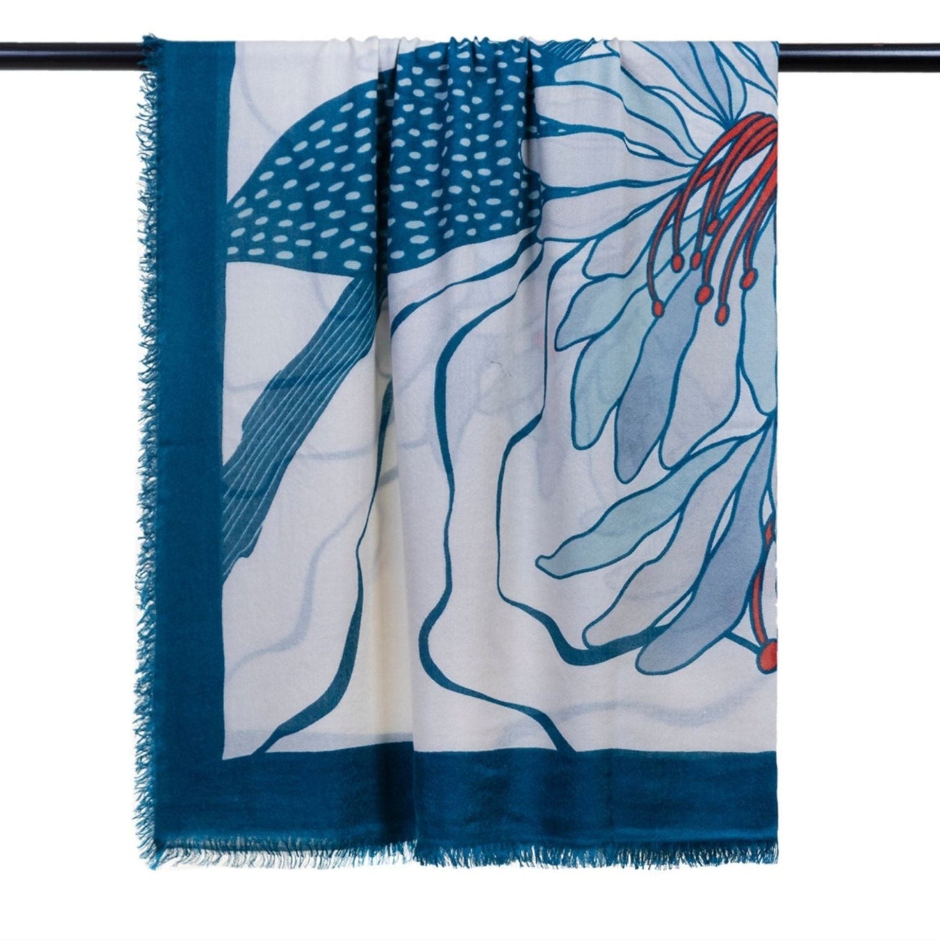 The Olympia Printed Square Scarf by OO-TO is a lightweight cashmere piece, handcrafted in Nepal with a teal combo border and abstract blue, white, and red floral design. Draped over a black rod, its frayed edges add relaxed elegance.