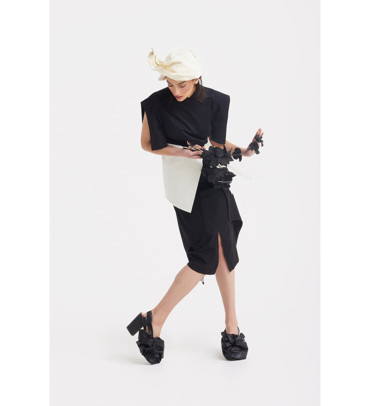 A person poses against a white background wearing the JULIA ALLERT Asymmetric Colour Block Top in black &amp; white, paired with large platform shoes, a white headpiece, and holding a black sculptural statement piece.