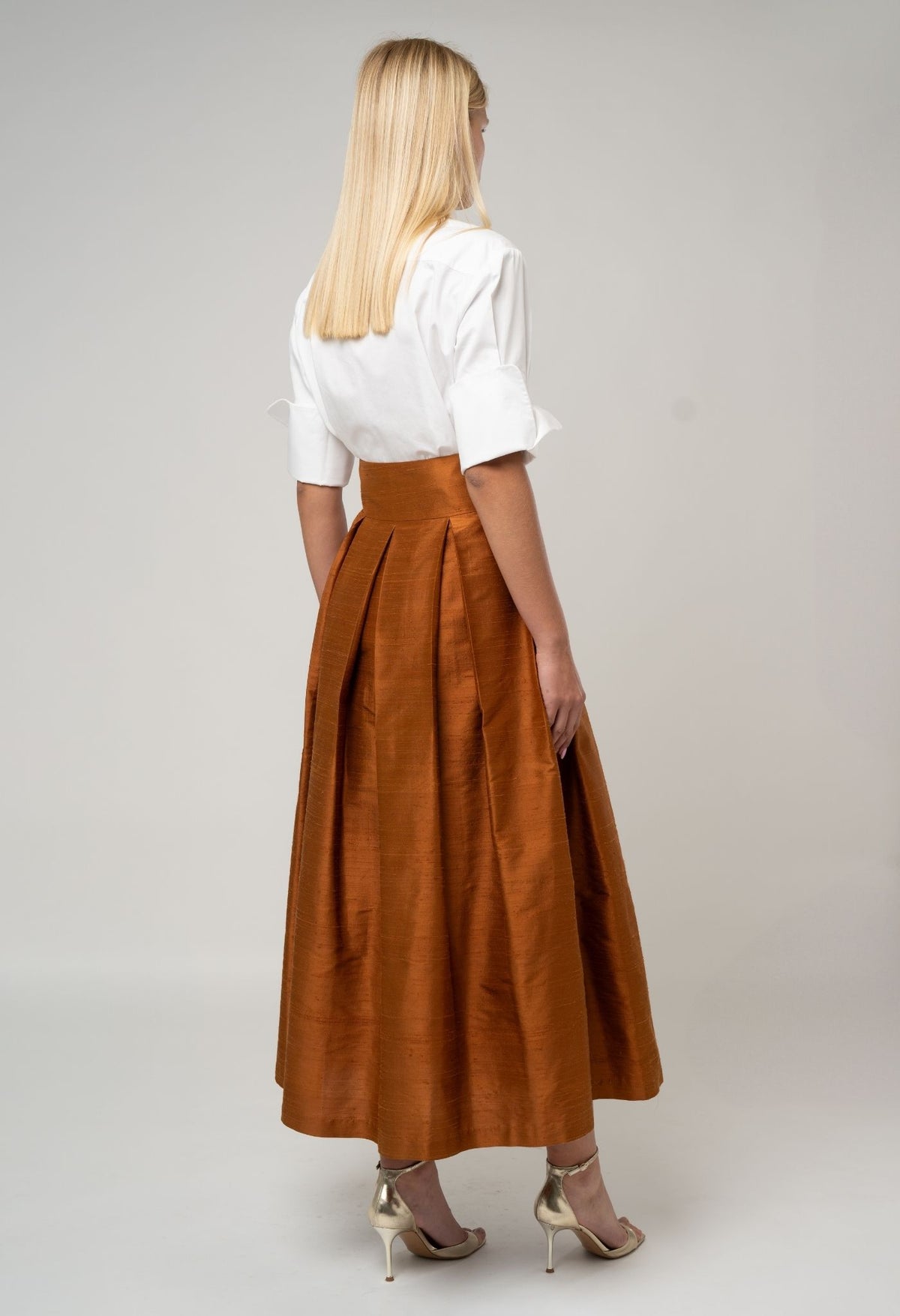 Woman wearing a white blouse and brown skirt on a plain background