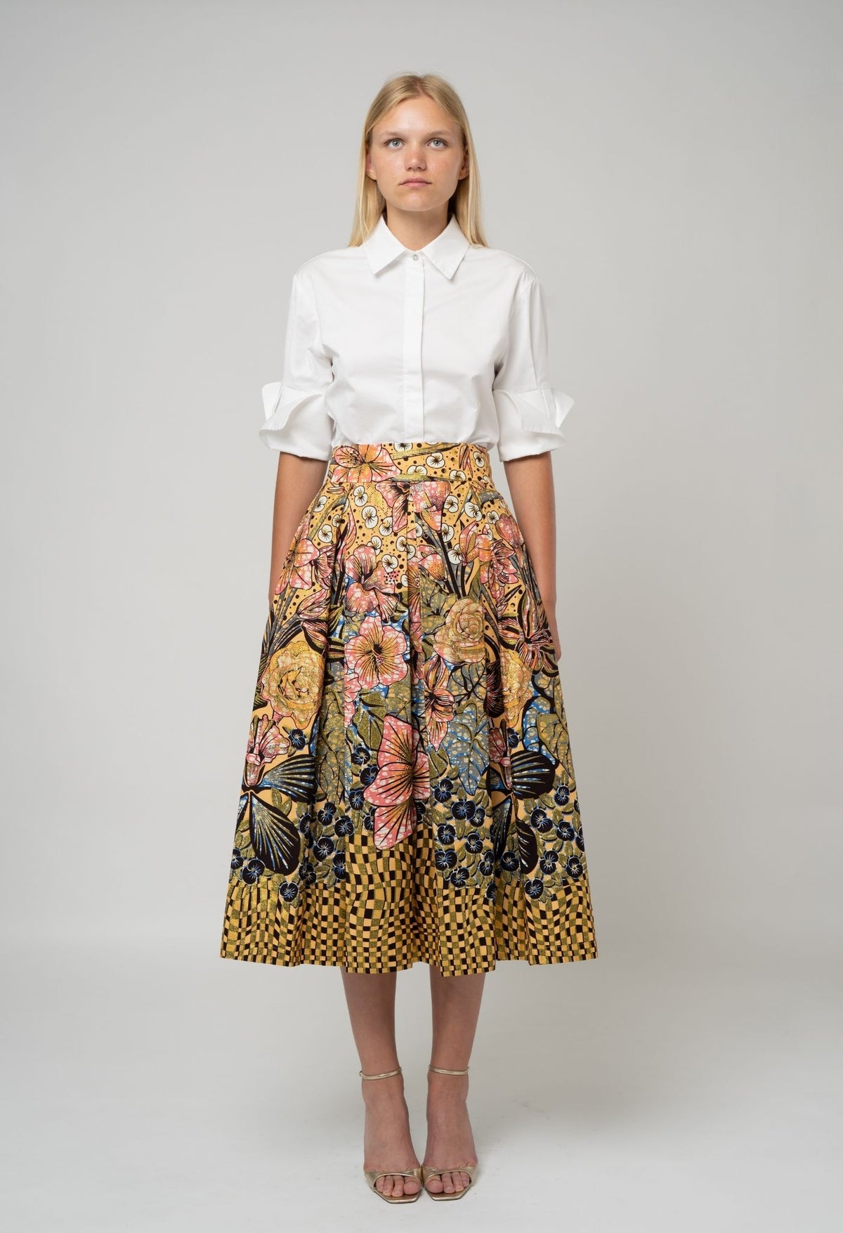 Woman wearing a white shirt and floral skirt on a plain background