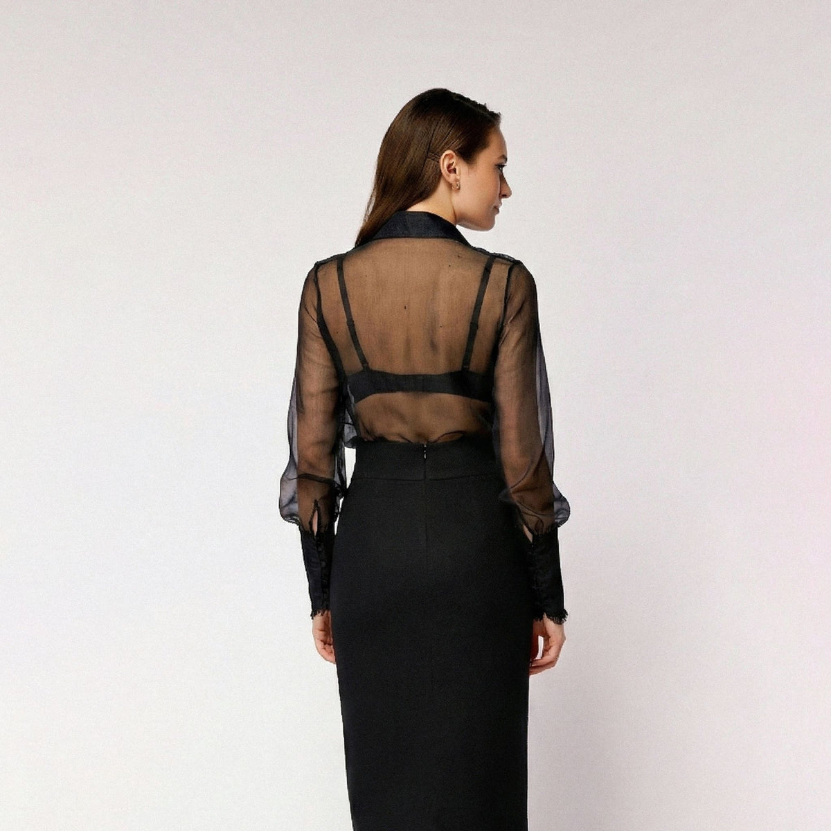Woman wearing a sheer black top over a long black dress on a white background