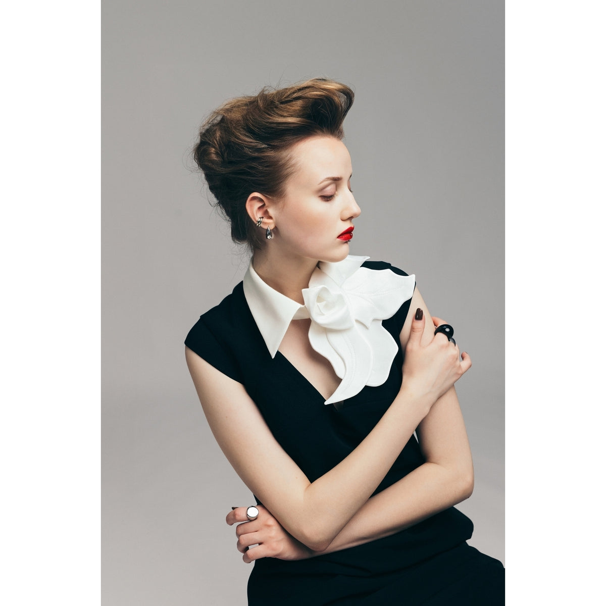 A woman with styled brown hair and red lipstick poses against a gray background, wearing the JULIA ALLERT Modern Business Sheath Dress With Decorative Collar in black, accessorized with rings and small earrings.