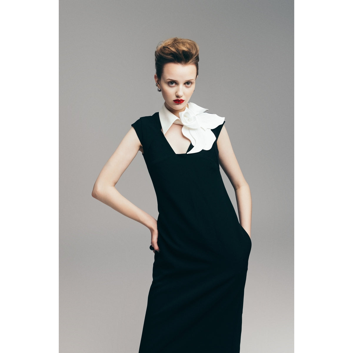 A woman in the JULIA ALLERT Modern Business Sheath Dress With Decorative Collar in black poses confidently against a light gray background, one hand on her hip, showcasing the dress&#39;s striking collar detail.