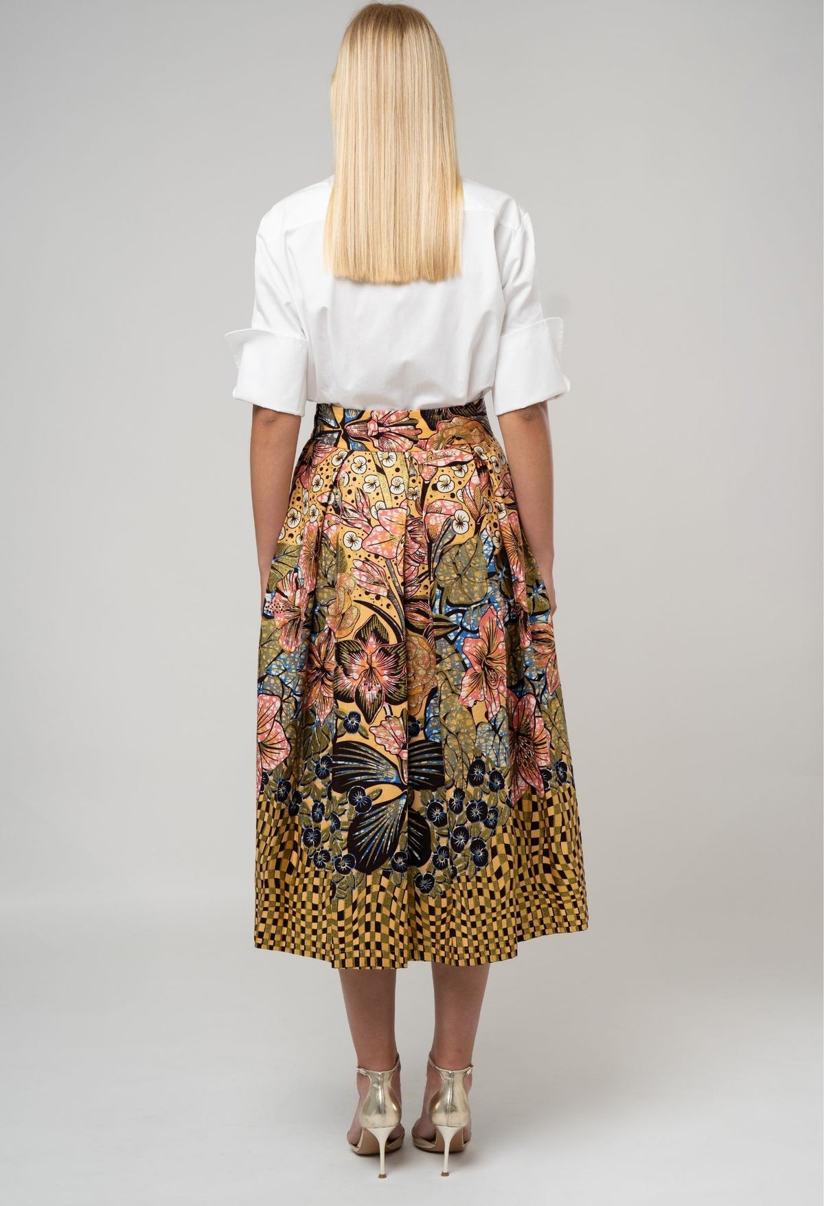 Woman wearing a white blouse and a colorful patterned skirt on a plain background