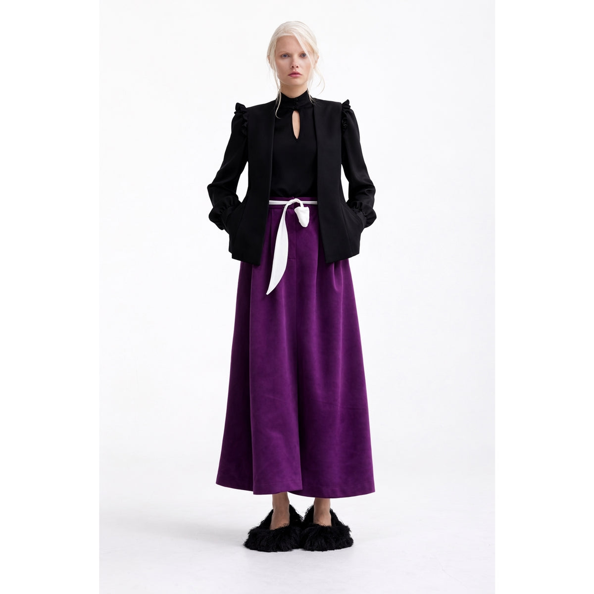 A woman with light blonde hair in a loose updo wears JULIA ALLERT’s Designer Satin Blouse With Bishop Sleeves And Stand Collar in black, styled elegantly with a blazer, long purple skirt, white belt, and black furry shoes. Perfect for any capsule wardrobe.
