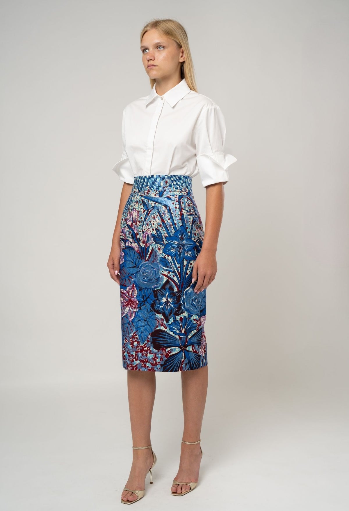 Woman wearing a white blouse and blue floral skirt on a plain background