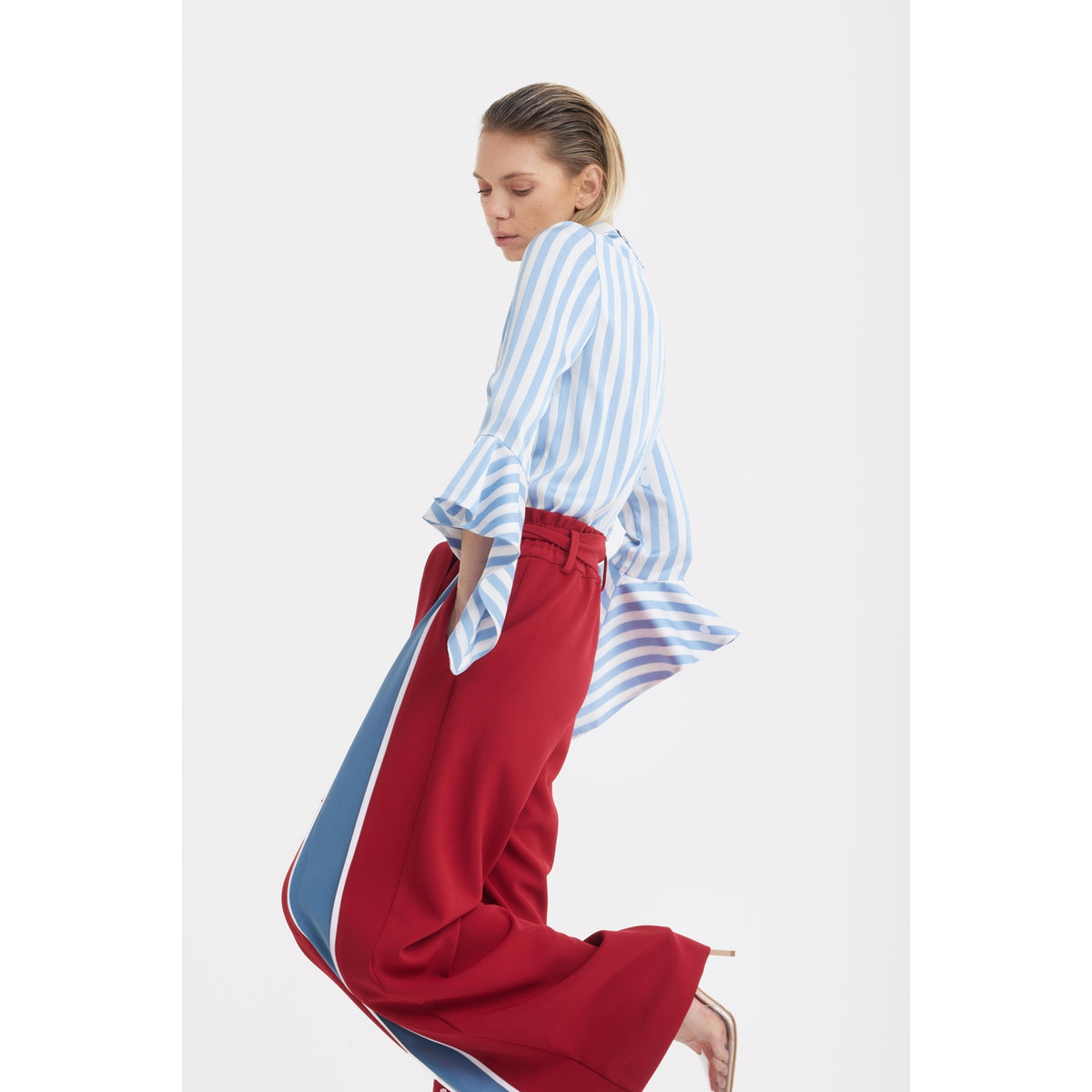 A person wearing the JULIA ALLERT Satin Striped Blouse With Asymmetric Collar in light blue and bright red wide-leg pants with blue and white side stripes poses against a plain white background.