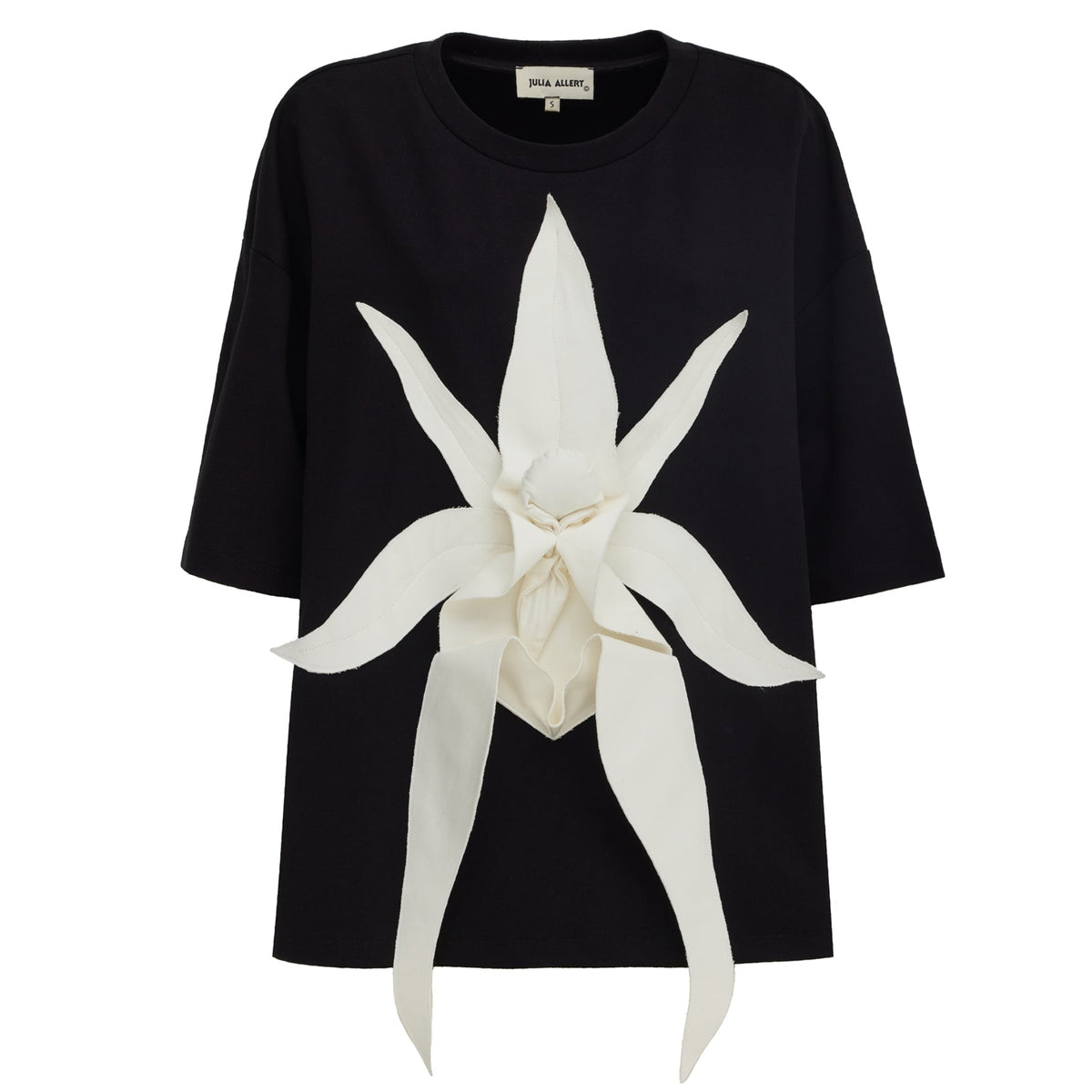 The JULIA ALLERT Relaxed Fit Knit Top - Black is a short-sleeve t-shirt featuring a sculptural floral appliqué: a large, three-dimensional white flower with elegantly extended petals at the center of the chest.
