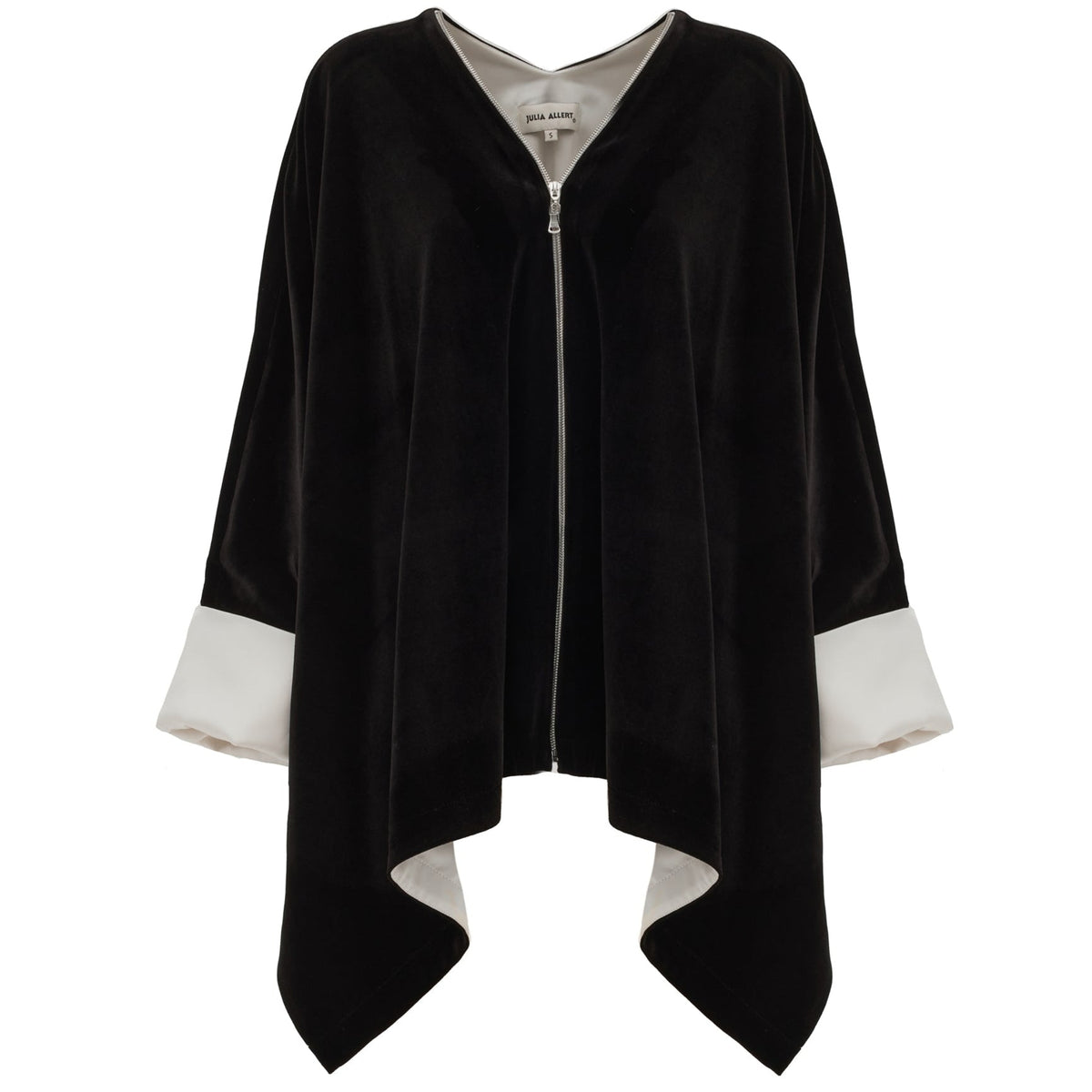 The JULIA ALLERT Loose Velvet Cape Jacket With Zip Front in black features wide white cuffs, an open zip front, asymmetrical hem, and visible collar label—an elegant choice for sophisticated evening layering.