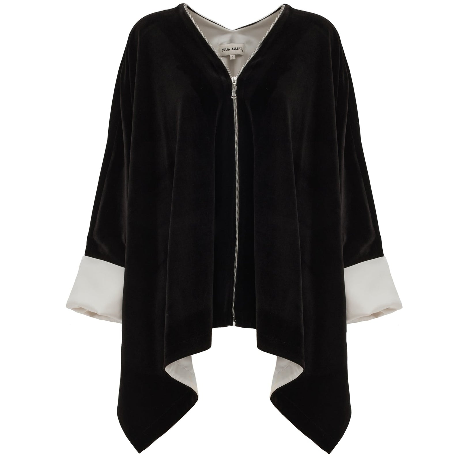 The JULIA ALLERT Loose Velvet Cape Jacket With Zip Front in black features wide white cuffs, an open zip front, asymmetrical hem, and visible collar label—an elegant choice for sophisticated evening layering.