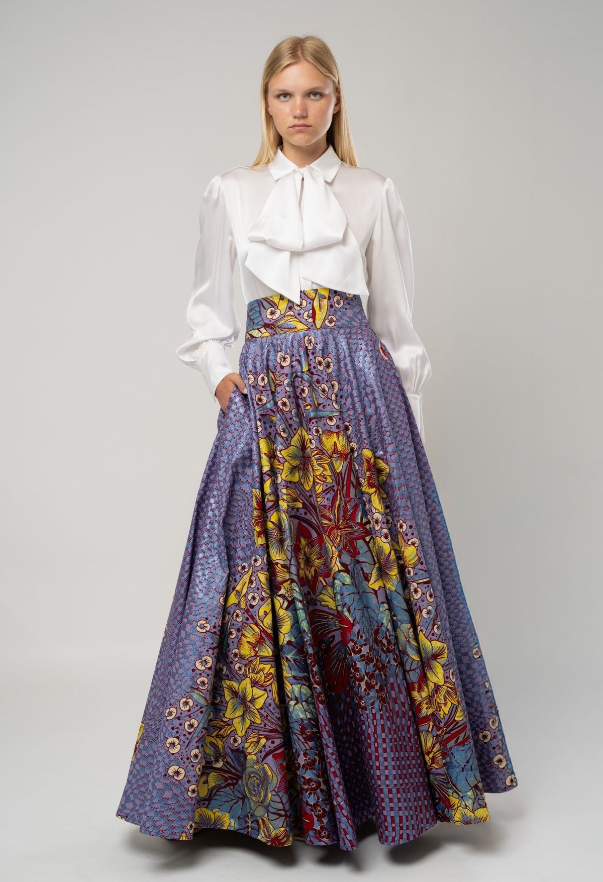 Woman wearing a white blouse and a long, colorful patterned skirt on a gray background