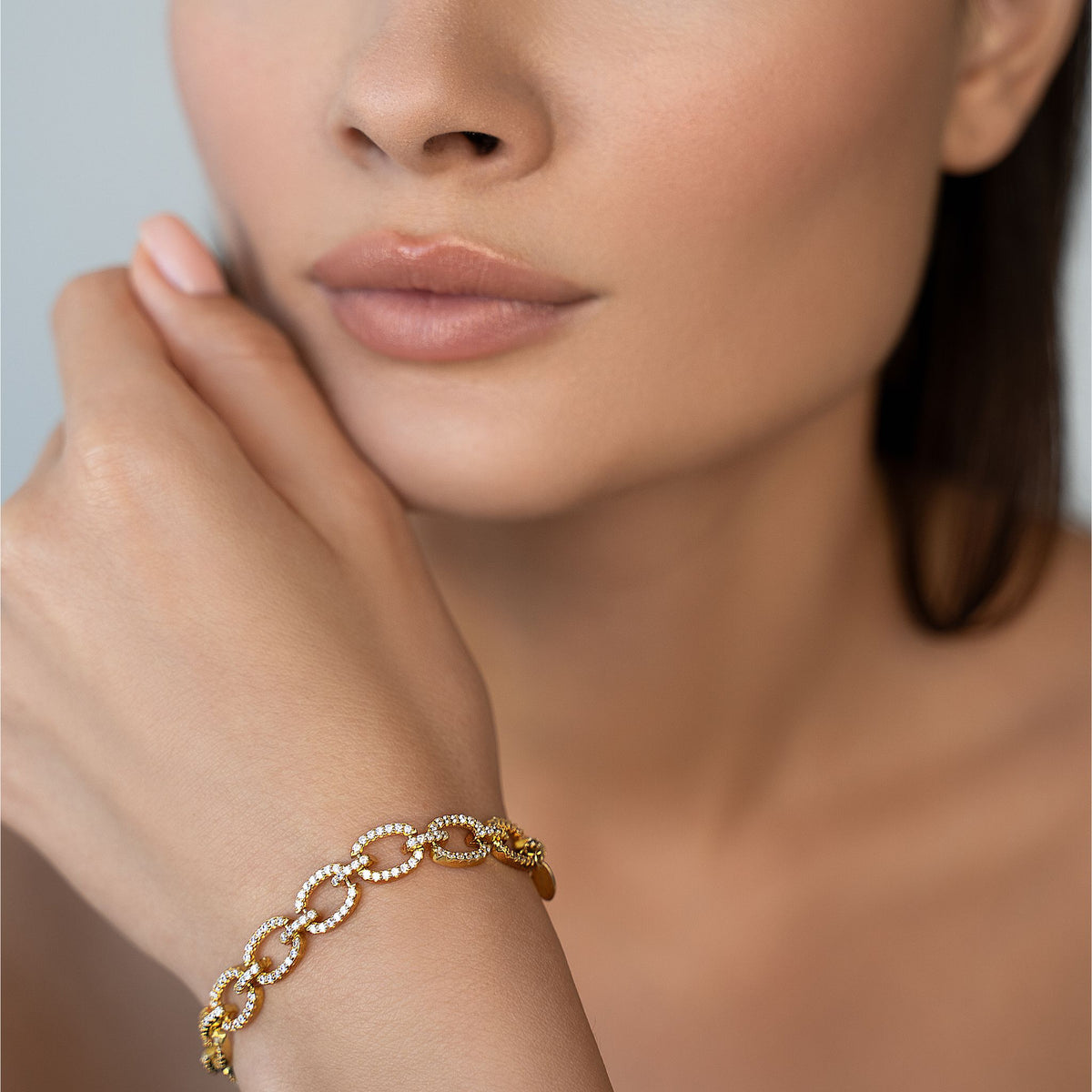 Close-up of a woman&#39;s hand wearing a gold bracelet with a neutral background