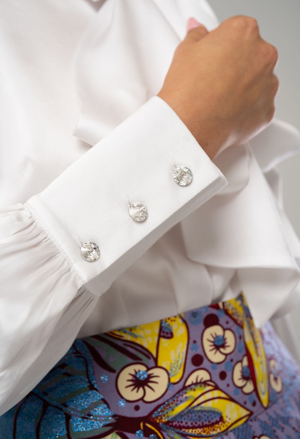 Close-up of a white shirt with decorative buttons and a colorful patterned fabric underneath.