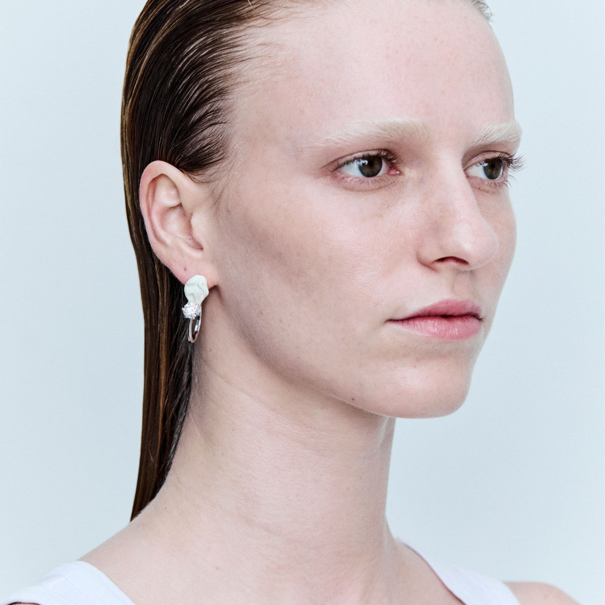 Close-up of a person wearing a white earring on a light gray background
