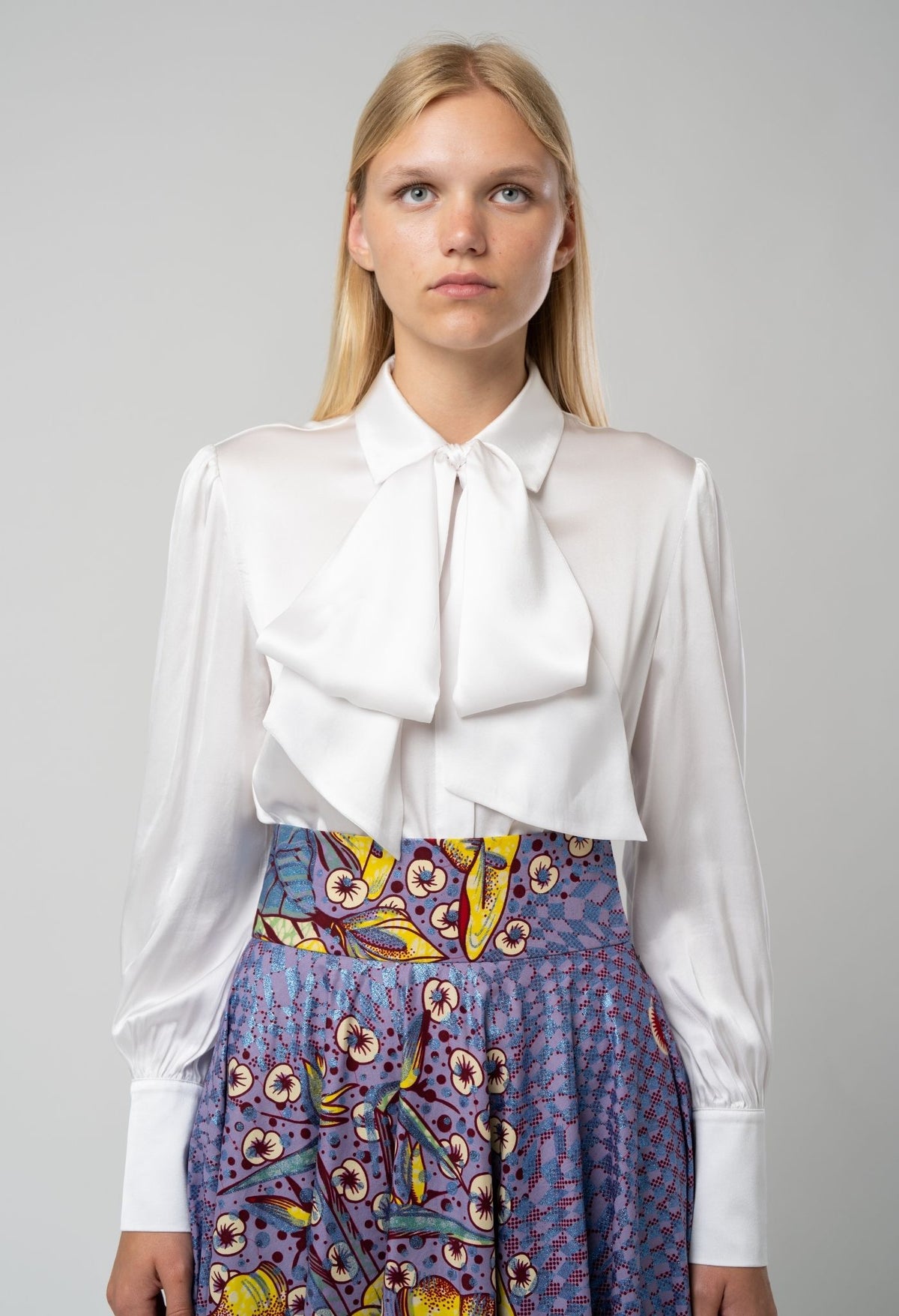 Woman wearing a white blouse with a bow and a colorful skirt on a gray background