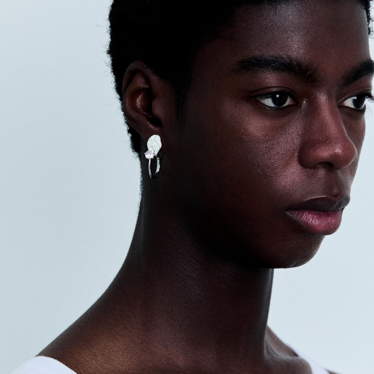 Close-up of a person wearing a white earring against a light gray background