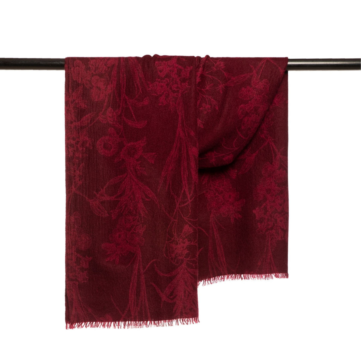 The OO-TO Modern Flower Printed Woven Cashmere Scarf in deep red, featuring a subtle floral pattern and fringed edges, is draped over a black rod against a white background—a statement of sustainable luxury.