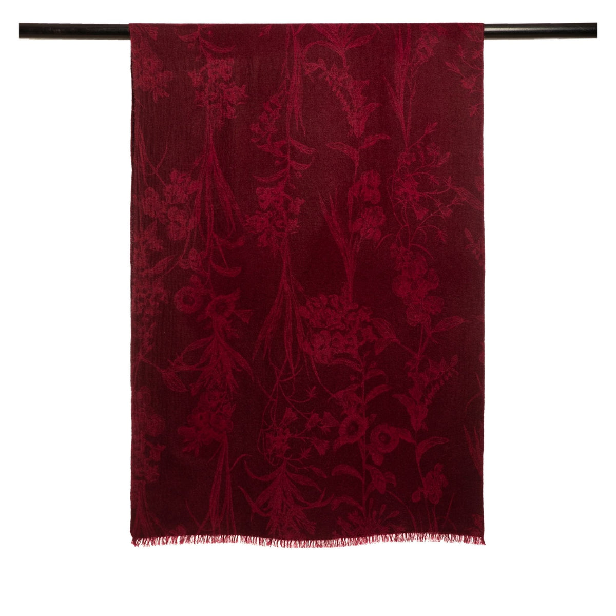 The OO-TO Modern Flower Printed Woven Cashmere Scarf in deep red, featuring a subtle floral pattern and short fringe, showcases sustainable luxury with its soft Himalayan cashmere and hangs elegantly over a black rod.