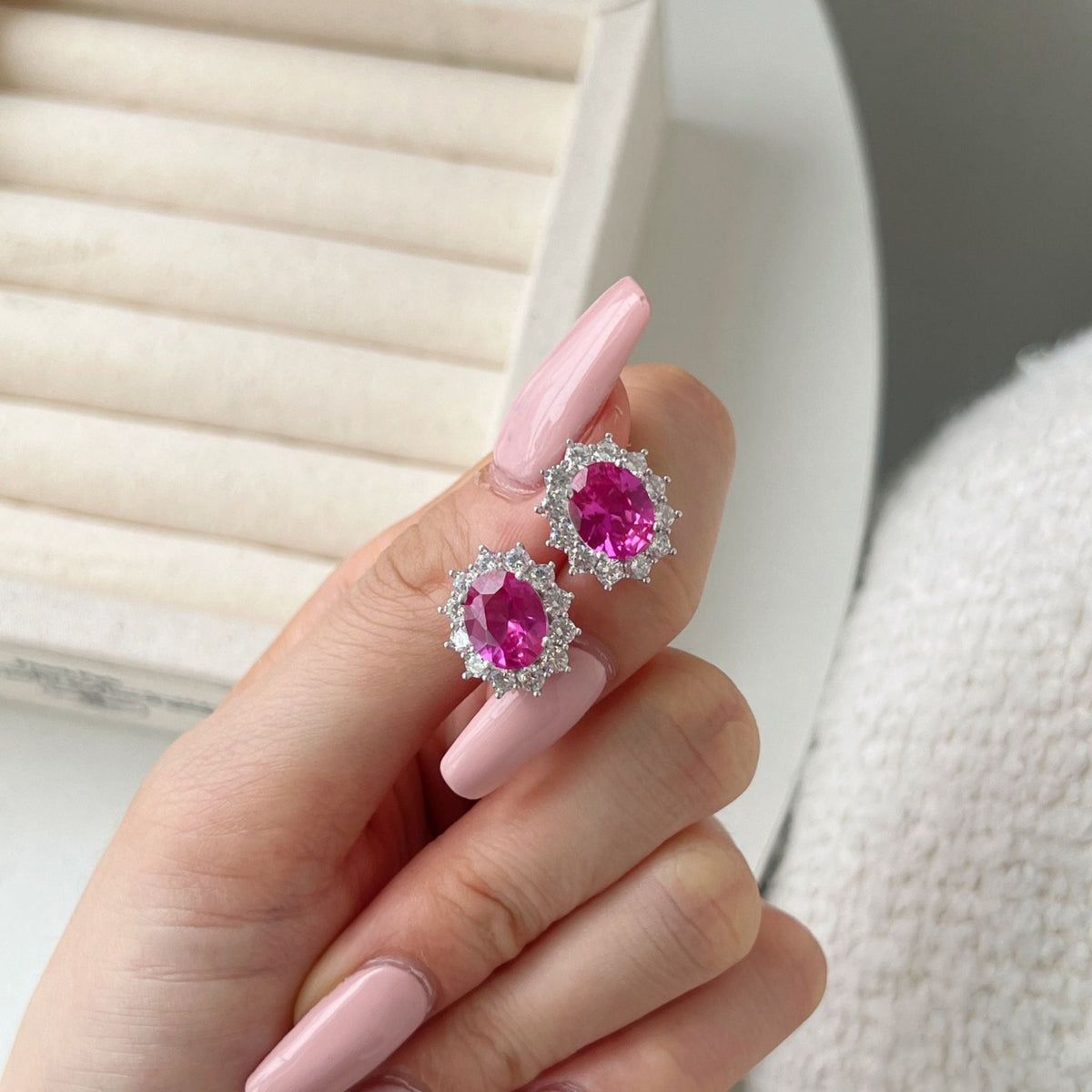 Pink gemstone earrings held by a hand with pink nail polish against a neutral background