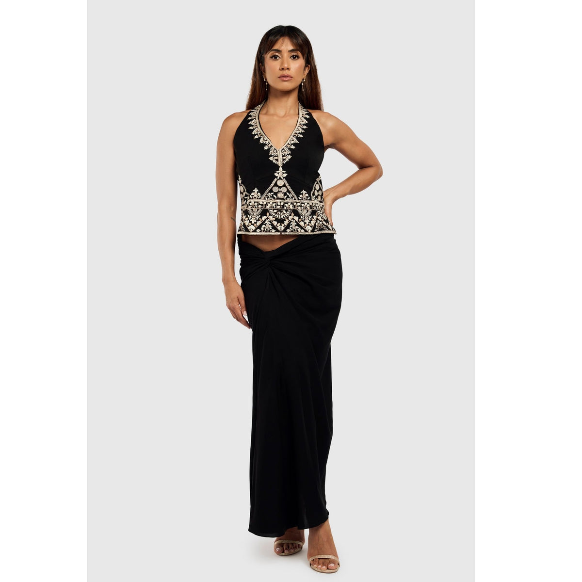 A woman exudes effortless elegance in INTERNATIONAL APPEAL’s Black Sari-Draped Maxi Skirt (PR Sample), styled with a sleeveless black top with white and gold embroidery, open-toed heels, long hair, and neutral makeup for a modern sari-inspired look.