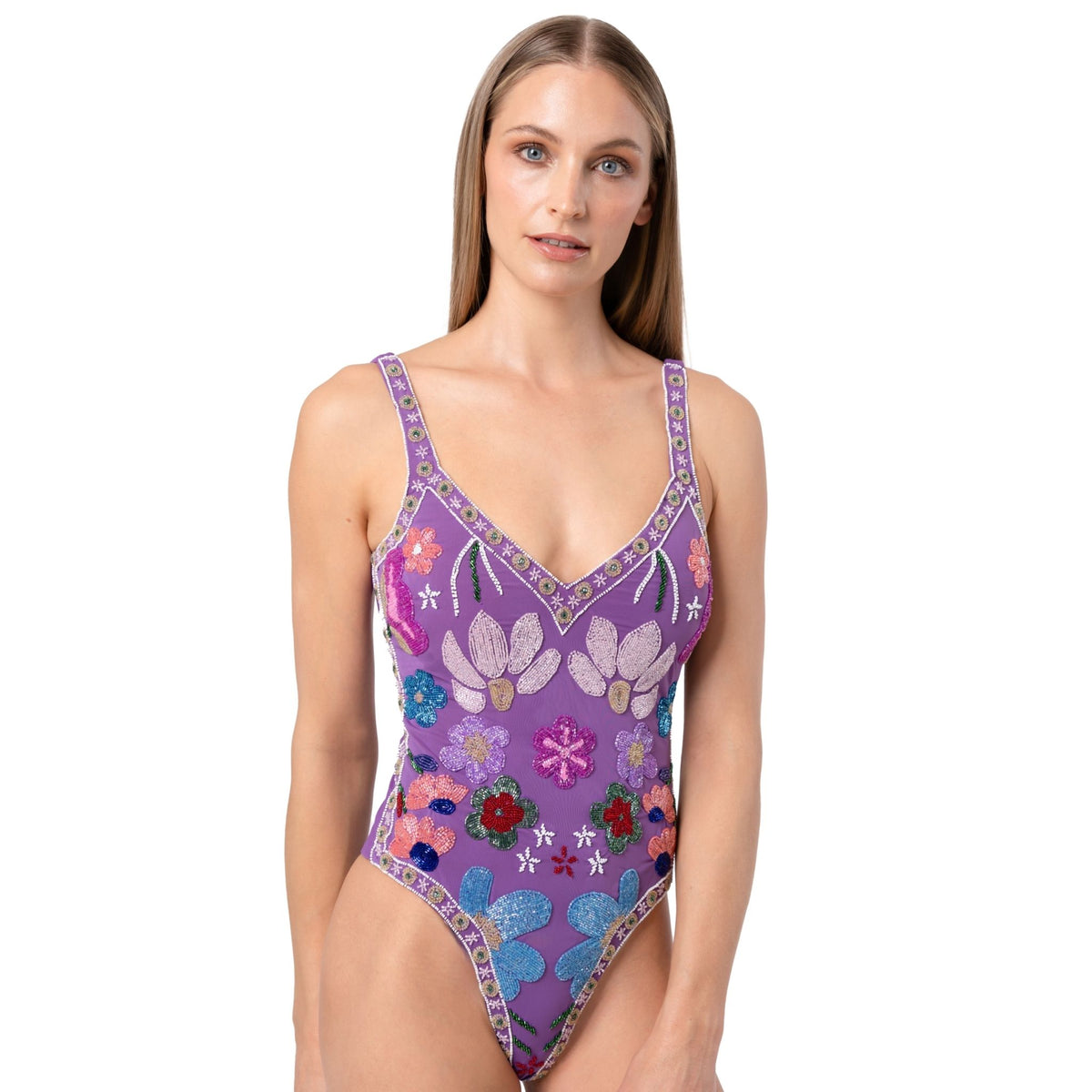 A woman with long straight hair models the SELF-ADORE Flower Hand-Beaded Embellished One-Piece Swimsuit in purple, featuring a floral pattern, V-neck, and thin straps, against a plain white background.