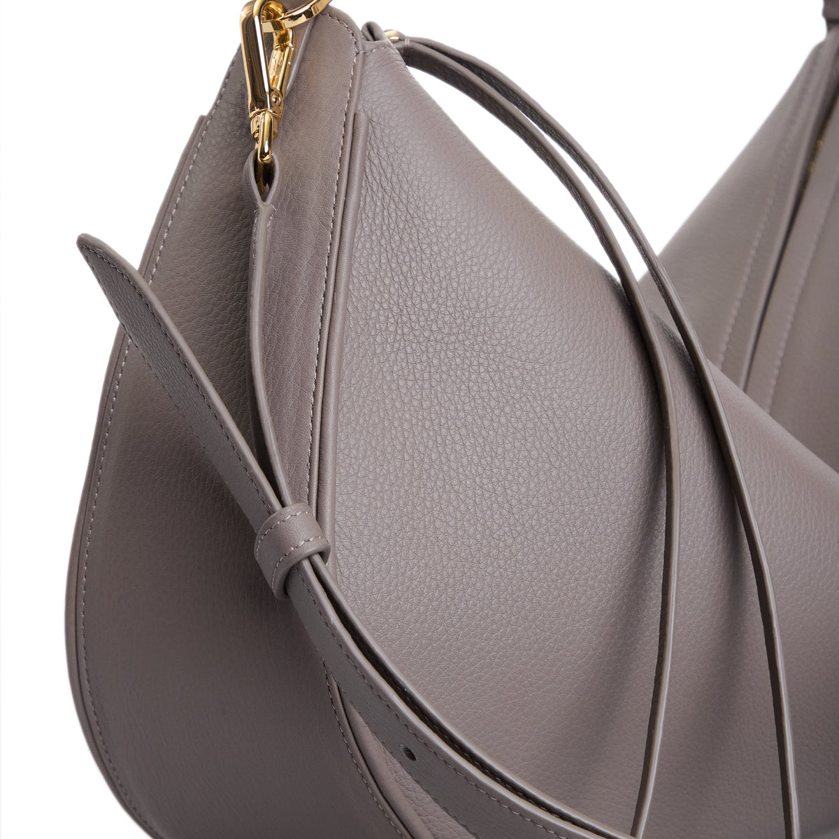 Close-up of the VIKELE STUDIO Denise Bag in gray, featuring pebbled leather, a curved silhouette, slim shoulder strap, and gold hardware. Detailed stitching and texture showcase its luxury craftsmanship.