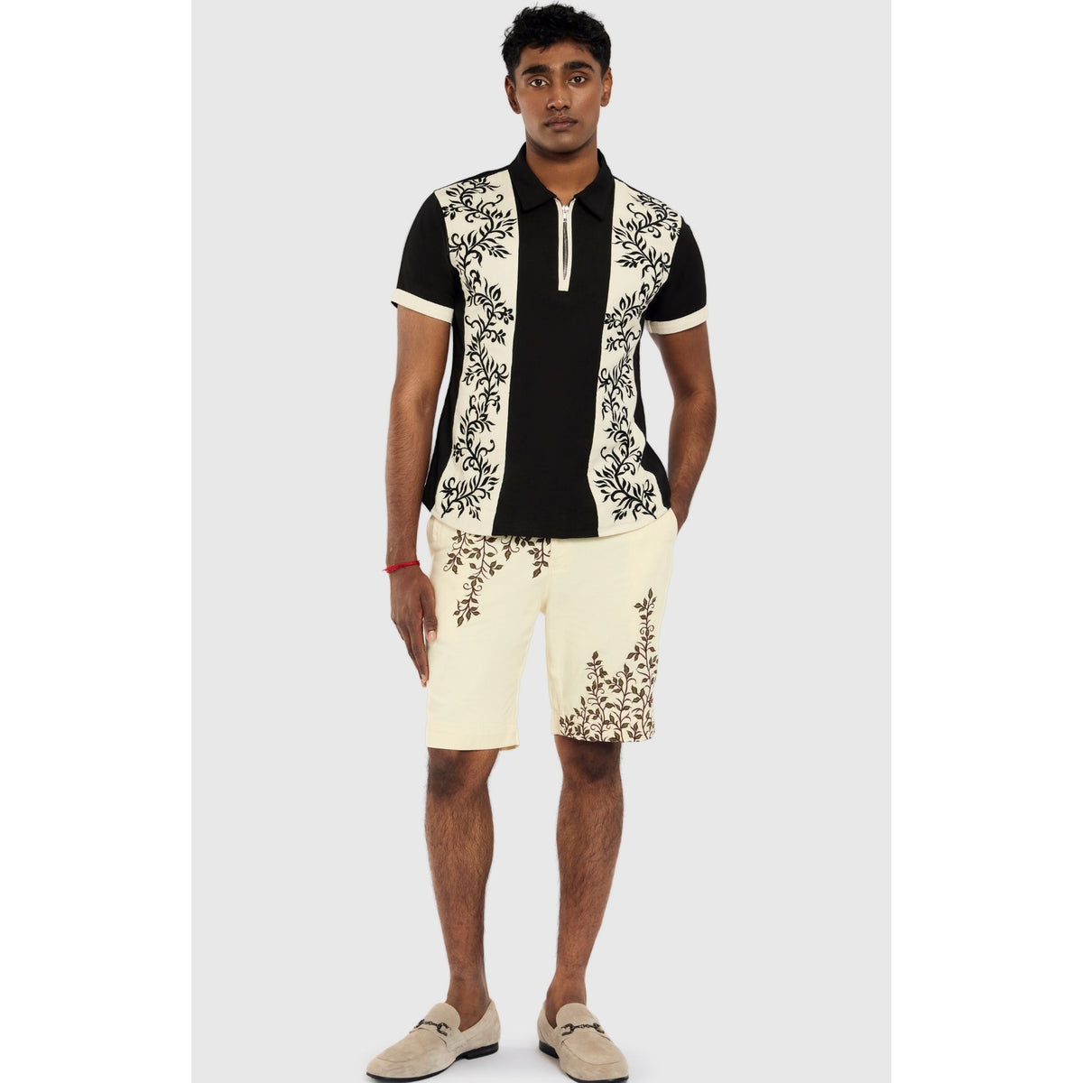 A man stands against a light gray background wearing INTERNATIONAL APPEAL’s Beige Vine Embroidered Shorts (PR Sample)—ideal for contemporary resort style.