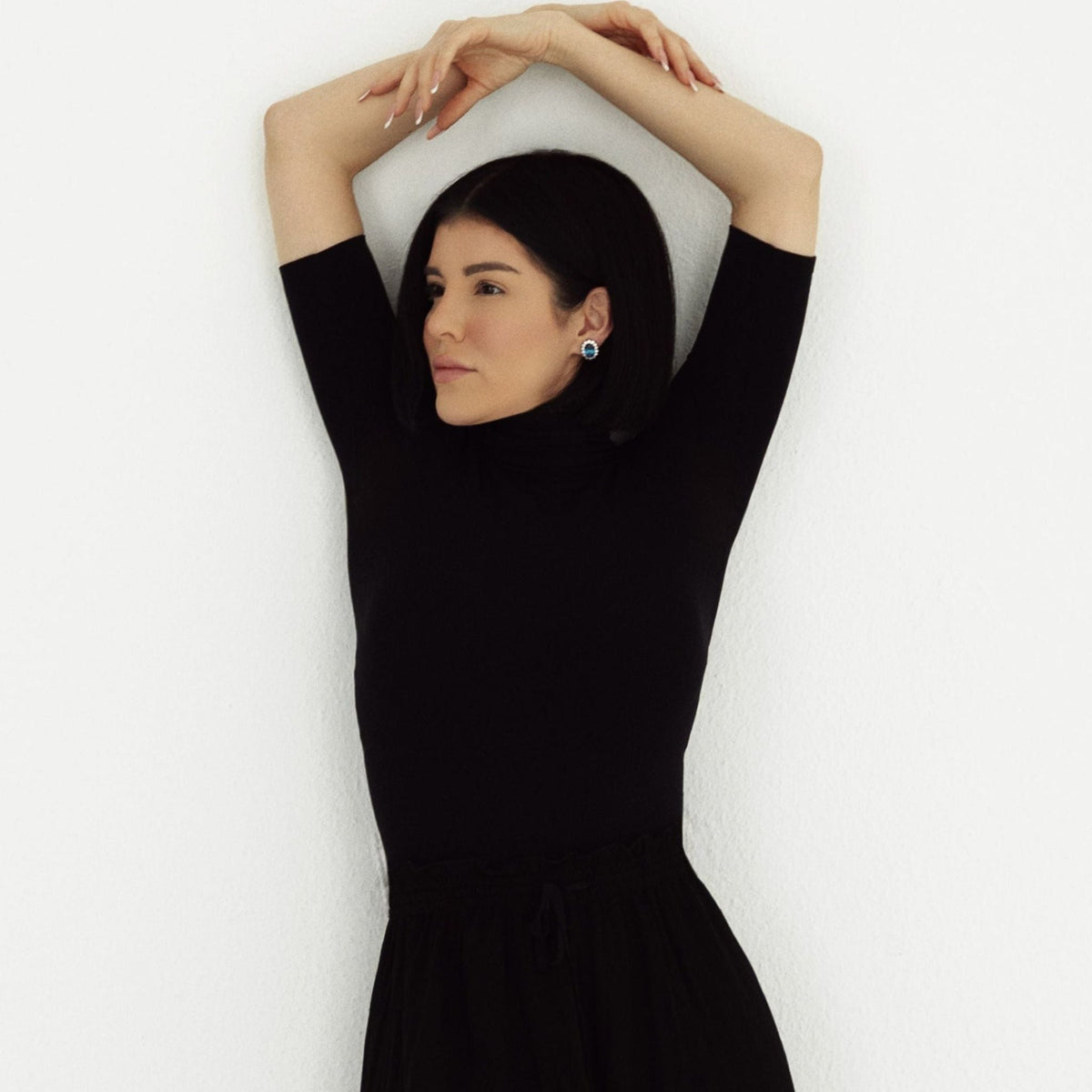 Woman wearing a black dress with her arms raised against a white background