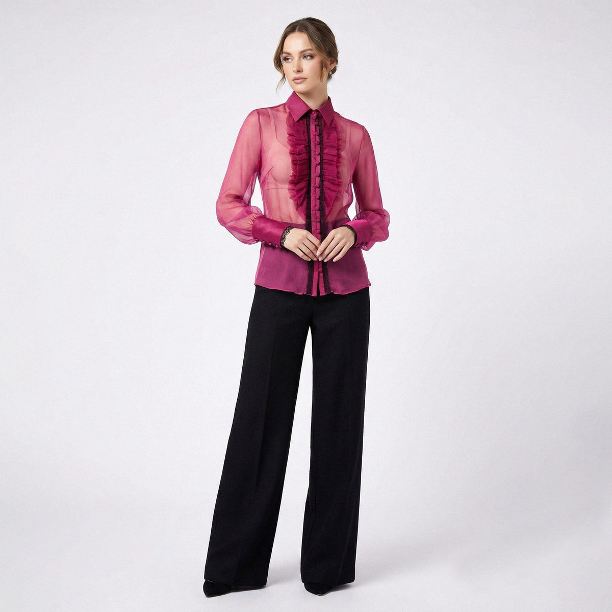 Woman wearing a pink blouse with ruffled details and black pants on a white background