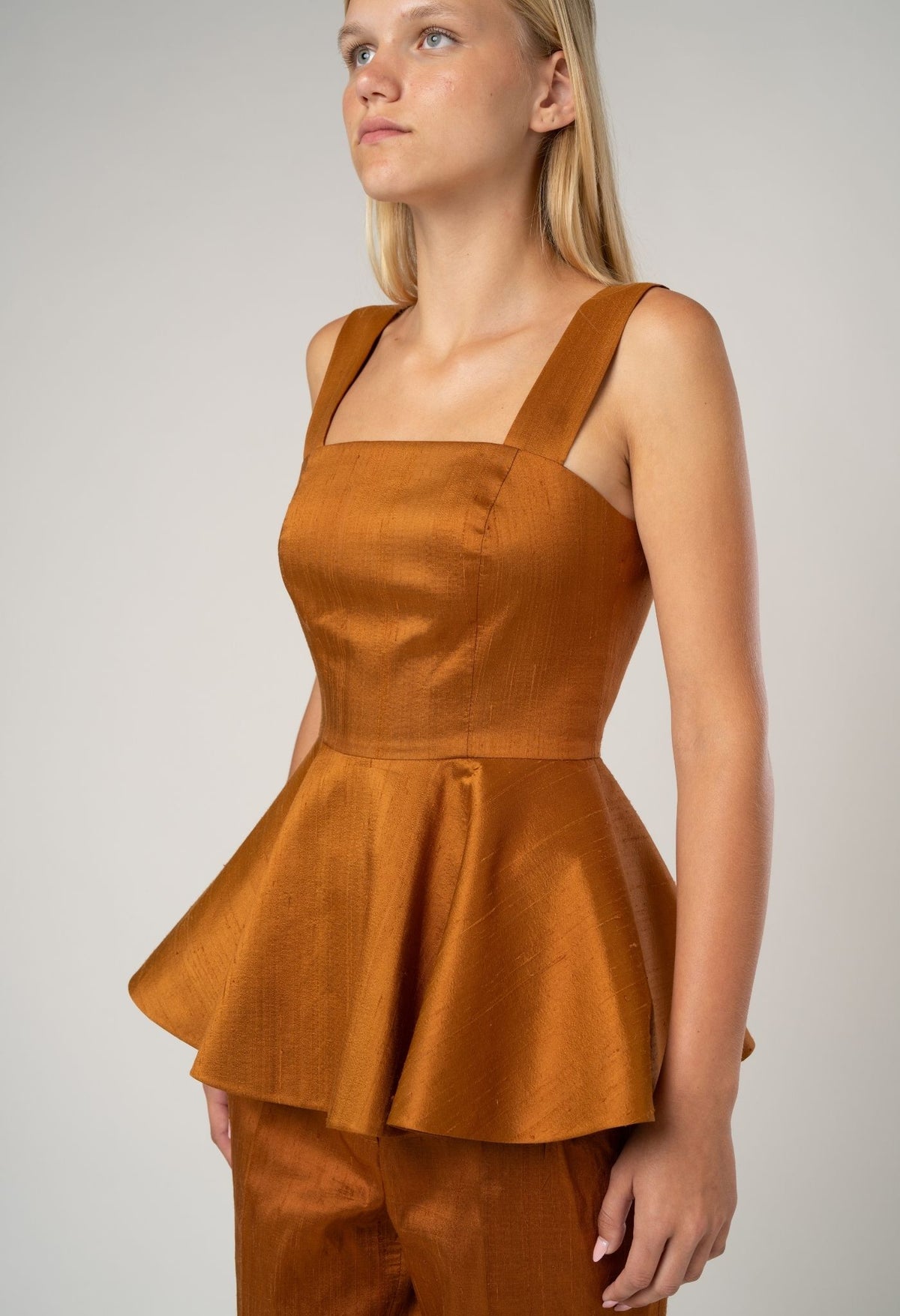 Woman wearing a brown peplum dress against a plain background
