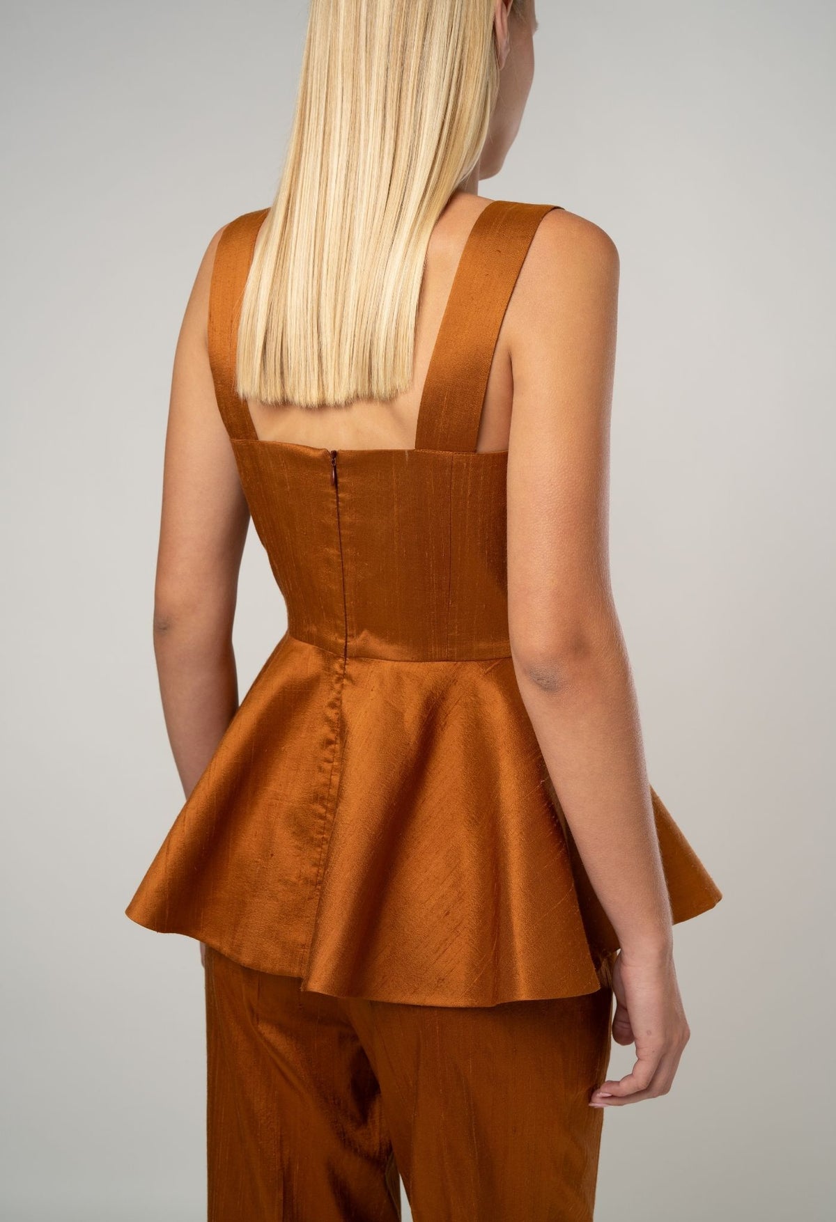 Person wearing a brown peplum top and pants on a plain background