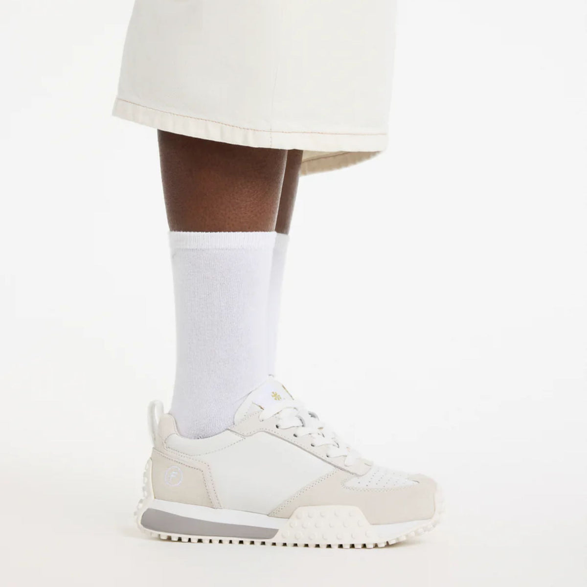 White sneaker worn with a white sock on a light gray background