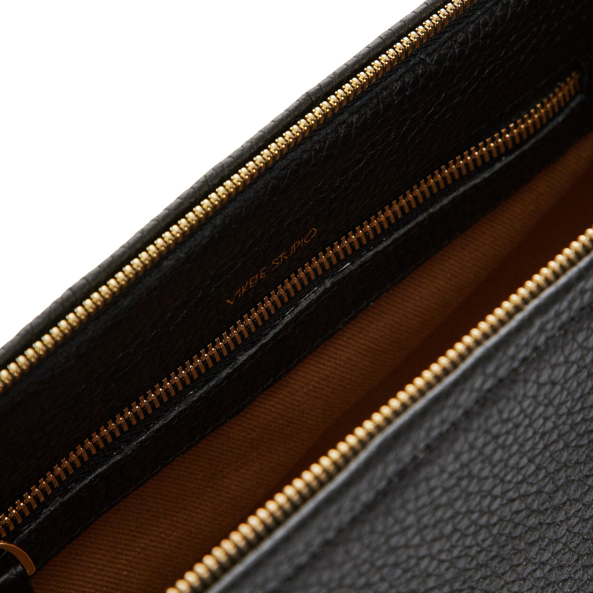 Close-up of the Denise Bag | Gray, an open gray leather bag with a gold zipper and brown lining. VIKELE STUDIO is printed in gold inside, showcasing this luxury handbag’s elegant details.
