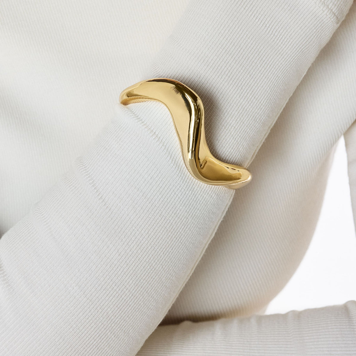 A person wearing a ribbed white top showcases the ANNA PRATA Gold Luma Bracelet from the Aviva Collection, a shiny, wave-shaped gold piece that embodies timeless jewelry elegance on their wrist.
