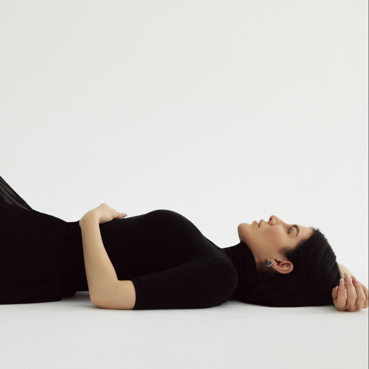 Woman lying on a white surface wearing a black outfit