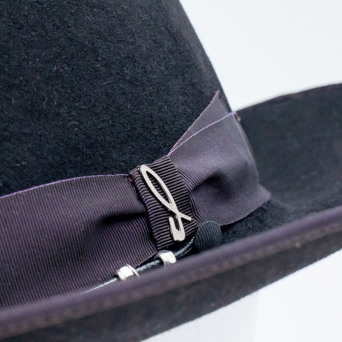 Close-up of a black hat with a purple ribbon and decorative pin on a white background