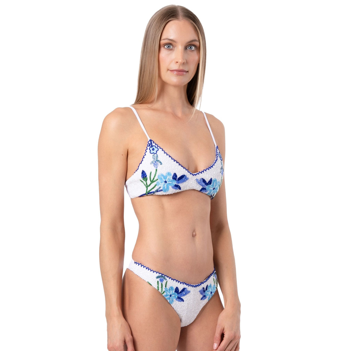 A woman with long, straight blonde hair models the SELF-ADORE Euro Summer Hand-Beaded Embellished Bikini Top in blue, standing against a plain white background for a chic European summer swimwear look.
