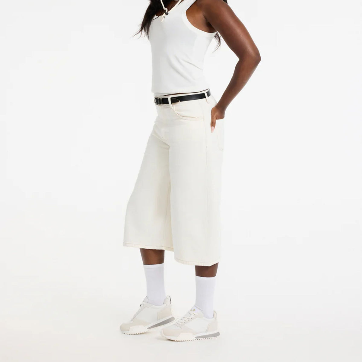 Person wearing a white sleeveless top and cream-colored wide-leg pants on a white background